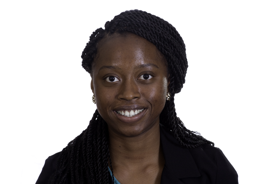 This Brian Charles Steel photo is a headshot of a woman of color.  She is wearing earrings and a black sweater over a green shirt. She has long hair in dreads.  She is centered in the frame, and the background is completely white.  She is lit in a Rembrandt style. 